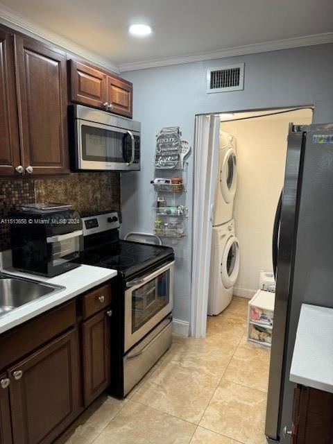 kitchen featuring stacked washer and dryer, light tile patterned floors, appliances with stainless steel finishes, decorative backsplash, and ornamental molding