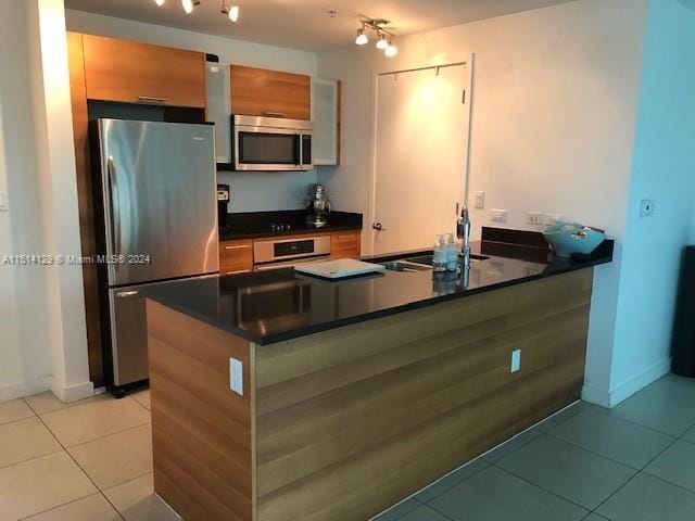 kitchen featuring stainless steel appliances, track lighting, light tile patterned floors, and kitchen peninsula