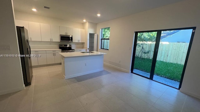 kitchen with light tile floors, stainless steel appliances, a kitchen island with sink, and white cabinetry