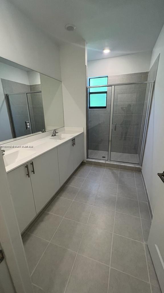 bathroom with an enclosed shower, double sink vanity, and tile flooring