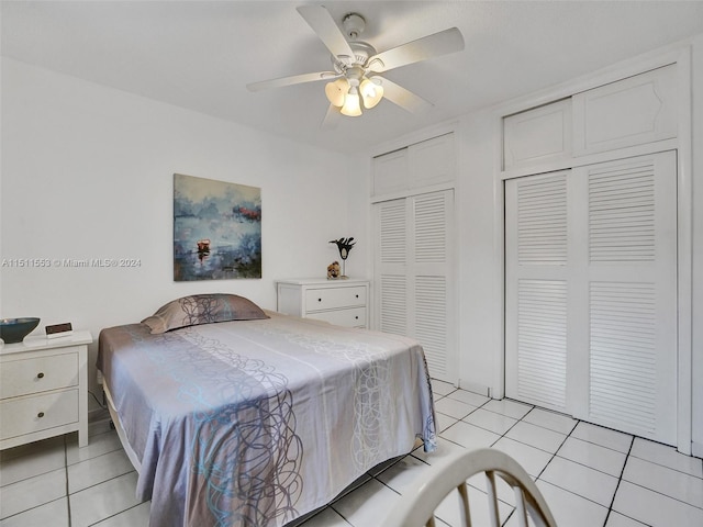 tiled bedroom with ceiling fan and two closets