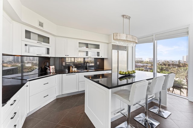 kitchen with hanging light fixtures, white cabinets, backsplash, sink, and dark tile patterned flooring