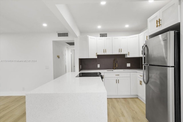 kitchen featuring tasteful backsplash, light hardwood / wood-style flooring, white cabinets, stainless steel refrigerator, and range