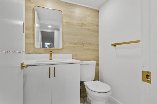 bathroom with toilet, vanity, and wood walls