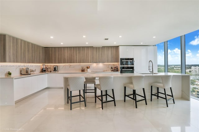 kitchen with white cabinets, light tile floors, a kitchen island with sink, and sink