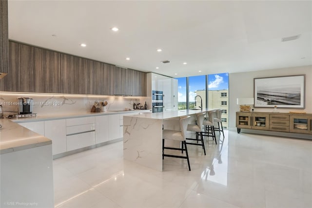 kitchen featuring a kitchen breakfast bar, a kitchen island with sink, white cabinets, and light tile floors