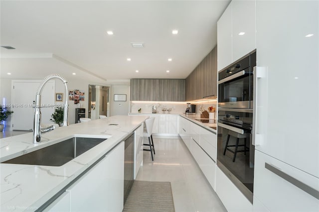 kitchen with white cabinets, light tile floors, sink, and light stone counters