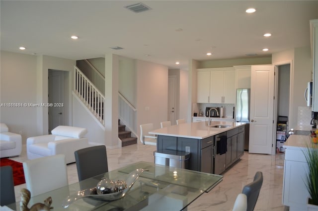 kitchen featuring backsplash, light tile flooring, sink, an island with sink, and white cabinets