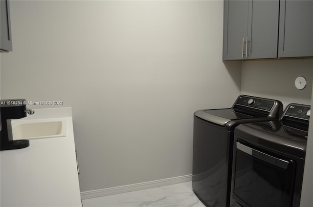 clothes washing area with light tile flooring, washing machine and dryer, cabinets, and sink