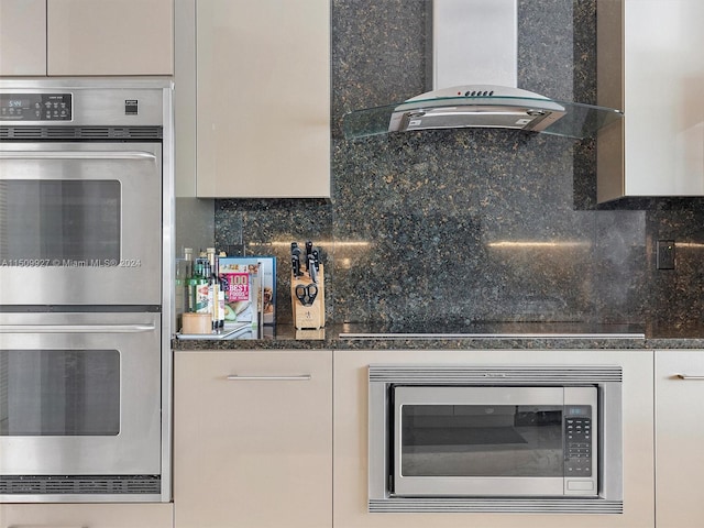 kitchen with wall chimney exhaust hood, tasteful backsplash, dark stone countertops, and stainless steel appliances