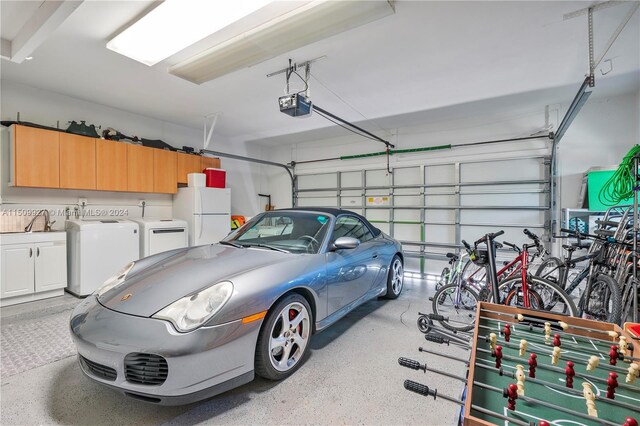 garage featuring sink, a garage door opener, washing machine and clothes dryer, and white refrigerator