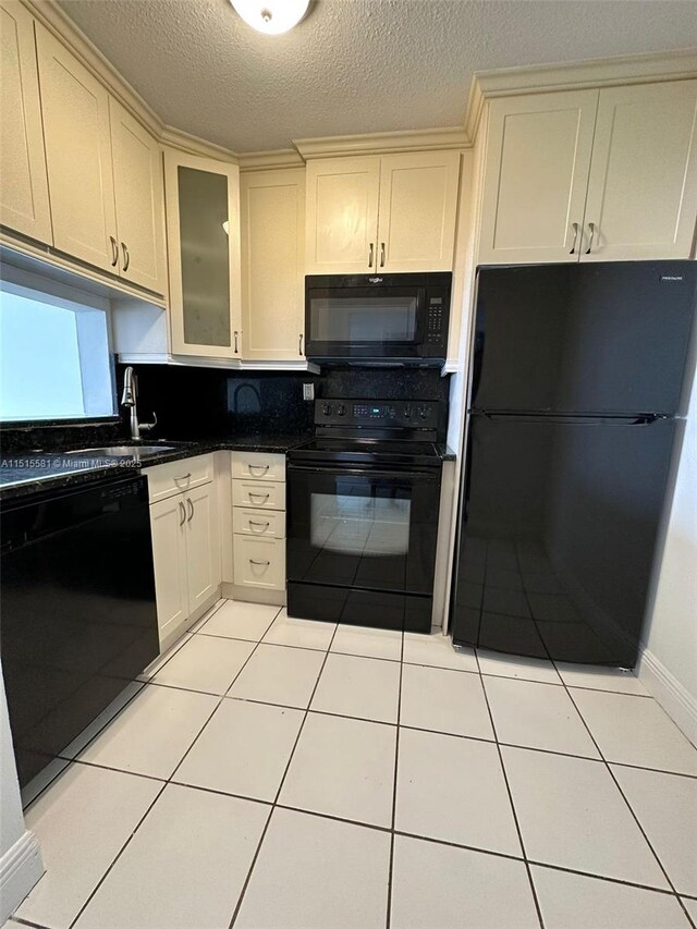 kitchen with black appliances, sink, light tile floors, a textured ceiling, and cream cabinetry