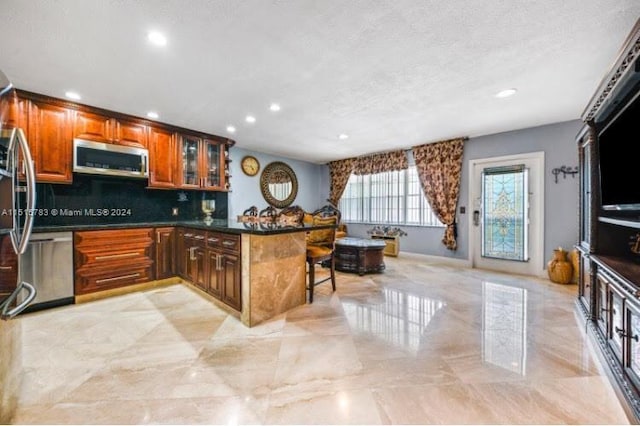 kitchen featuring backsplash, a kitchen breakfast bar, stainless steel appliances, light tile floors, and a textured ceiling