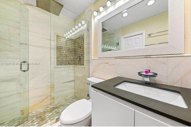 bathroom with toilet, large vanity, a shower with door, tile walls, and backsplash