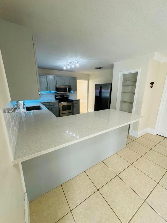 kitchen with kitchen peninsula, appliances with stainless steel finishes, light tile floors, and track lighting