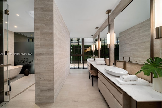 bathroom featuring tile patterned flooring, expansive windows, a tub to relax in, vanity, and tile walls