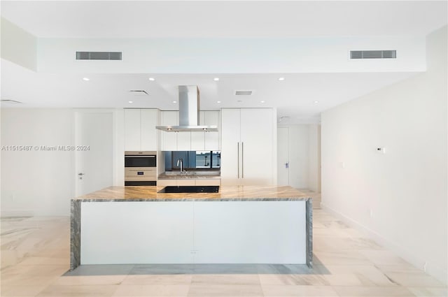 kitchen with light tile floors, light stone countertops, white cabinetry, and island range hood