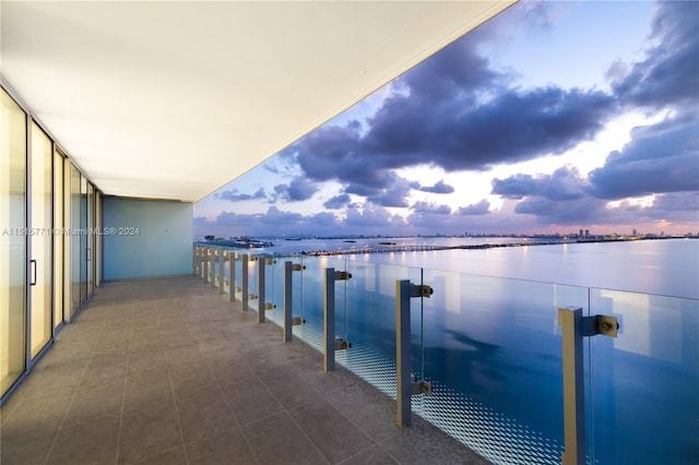 balcony at dusk featuring a water view