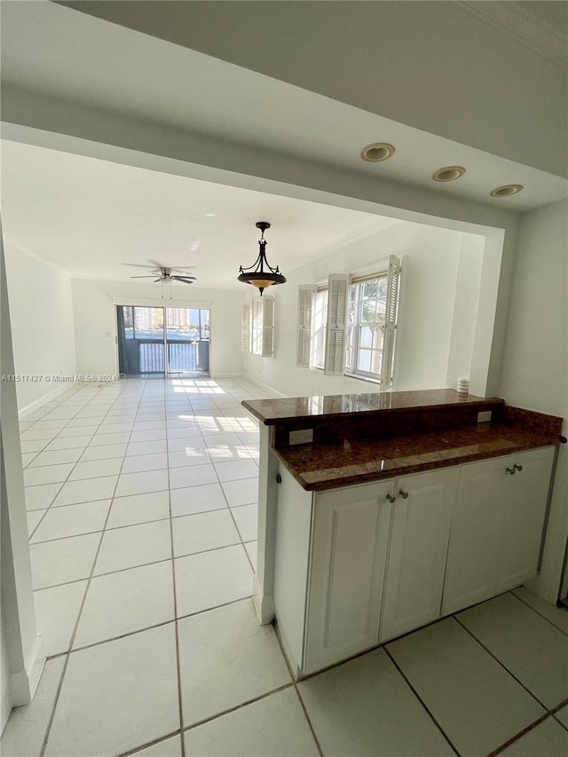 kitchen featuring ceiling fan, light tile floors, dark stone counters, hanging light fixtures, and white cabinets