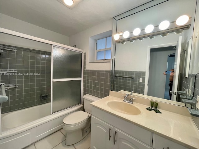 full bathroom with vanity, tile walls, combined bath / shower with glass door, tile floors, and toilet