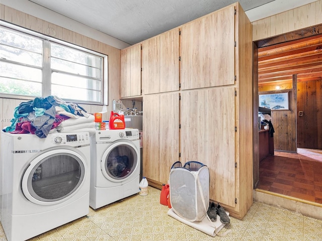 clothes washing area featuring cabinets, light tile patterned floors, wooden walls, and washing machine and clothes dryer