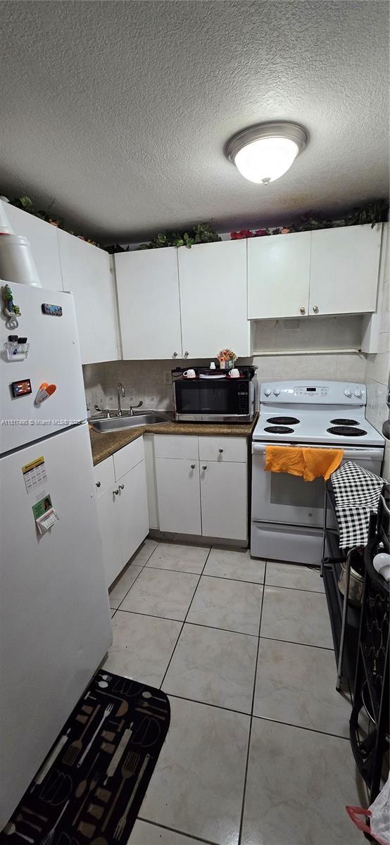 kitchen featuring sink, white appliances, light tile patterned floors, a textured ceiling, and white cabinets