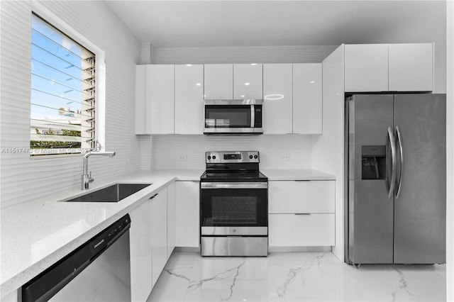 kitchen with appliances with stainless steel finishes, white cabinetry, light stone countertops, and sink