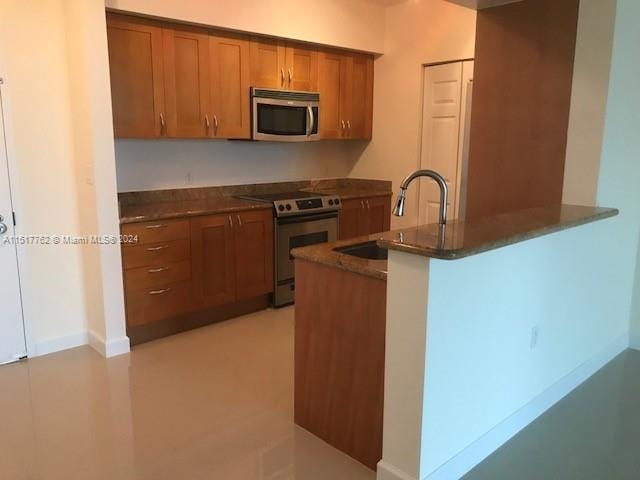 kitchen with kitchen peninsula, stainless steel appliances, sink, and dark stone counters