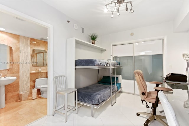 tiled bedroom with tile walls, a closet, and ensuite bathroom