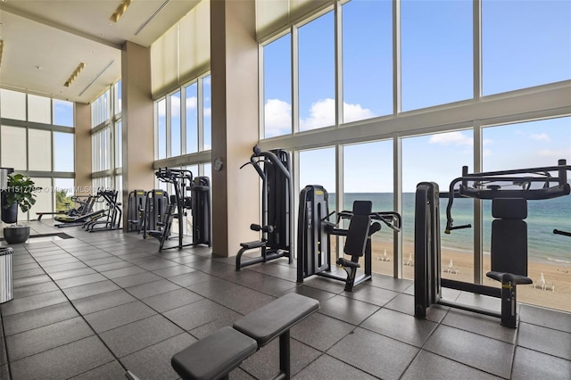 exercise room featuring dark tile flooring, a water view, and a high ceiling