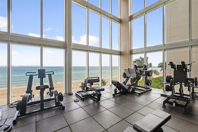 gym with a water view, a high ceiling, a healthy amount of sunlight, and a view of the beach