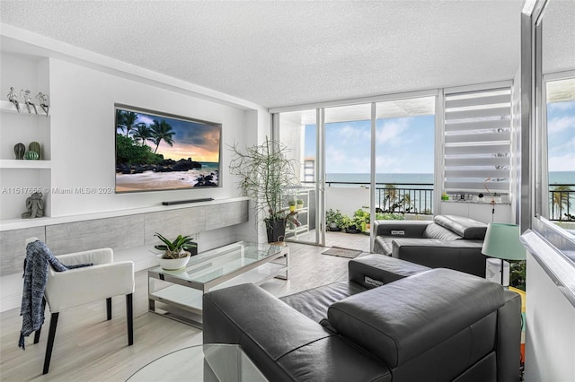 living room featuring a water view, expansive windows, a textured ceiling, and light wood-type flooring