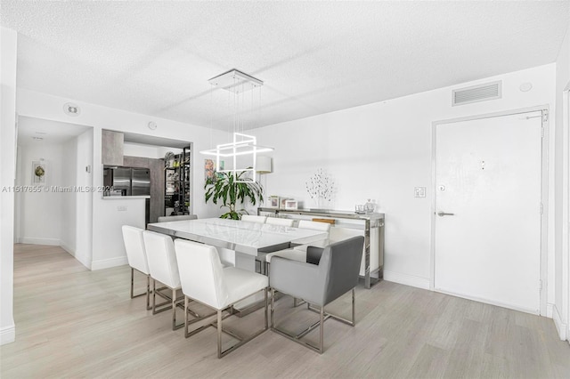 dining space featuring a notable chandelier, a textured ceiling, and light wood-type flooring