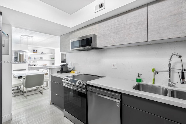 kitchen with hanging light fixtures, stainless steel appliances, sink, and light stone counters