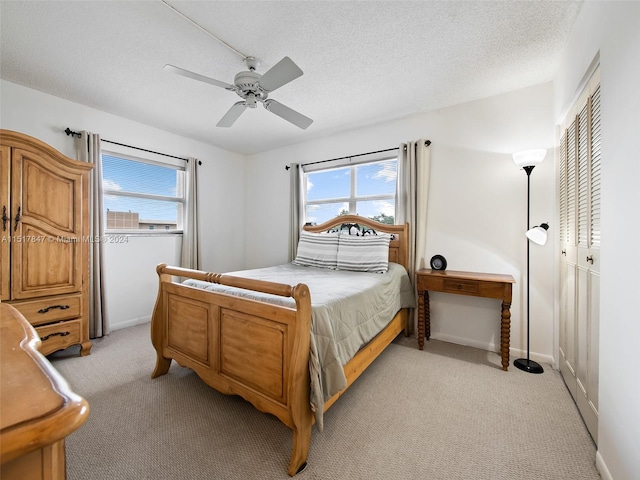 bedroom featuring ceiling fan, a closet, light colored carpet, and a textured ceiling