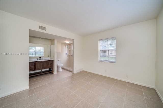 bedroom with ensuite bath, light tile floors, and sink