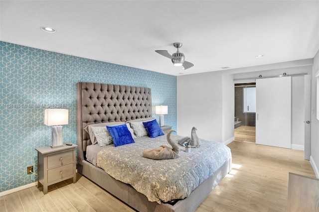 bedroom featuring a barn door, ceiling fan, and light wood-type flooring