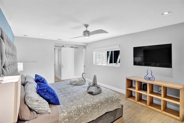 bedroom with a barn door, ceiling fan, and light wood-type flooring