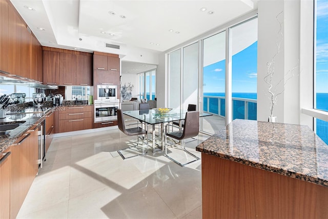 kitchen with dark stone counters, light tile flooring, custom exhaust hood, a water view, and a center island