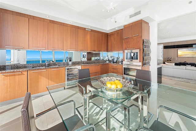 kitchen featuring double oven, a kitchen breakfast bar, sink, dark stone countertops, and beverage cooler