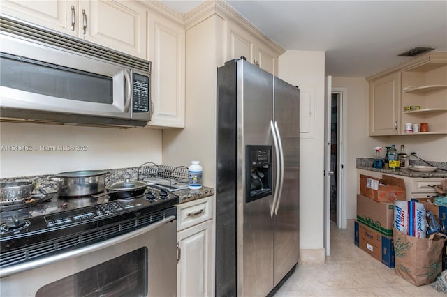 kitchen with cream cabinets, stainless steel appliances, and dark stone counters