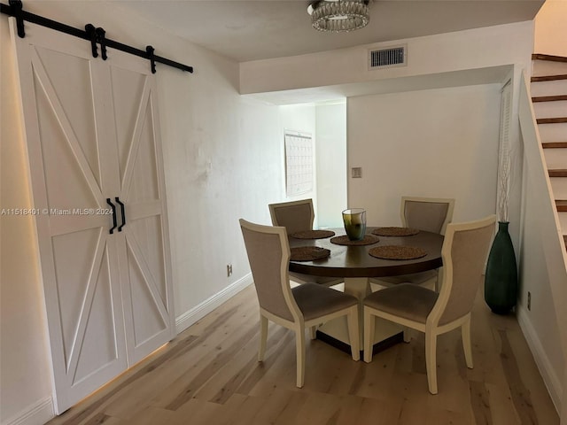 dining space with a barn door, an inviting chandelier, and light wood-type flooring