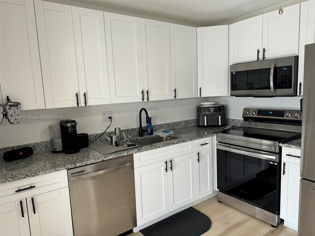 kitchen featuring white cabinetry, light hardwood / wood-style floors, sink, stainless steel appliances, and dark stone counters