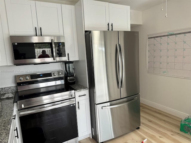 kitchen featuring white cabinets, light wood-type flooring, dark stone countertops, and appliances with stainless steel finishes