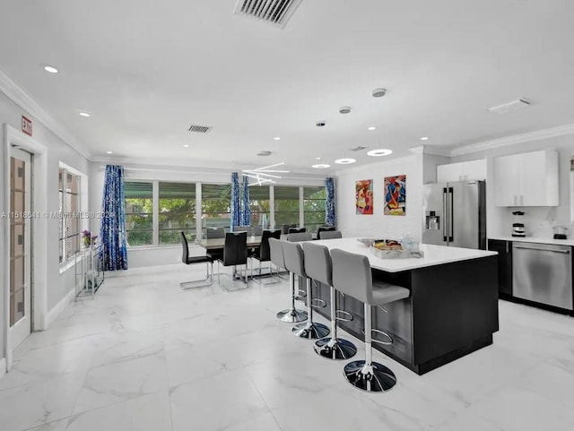 kitchen featuring stainless steel appliances, a center island, a kitchen bar, ornamental molding, and white cabinets