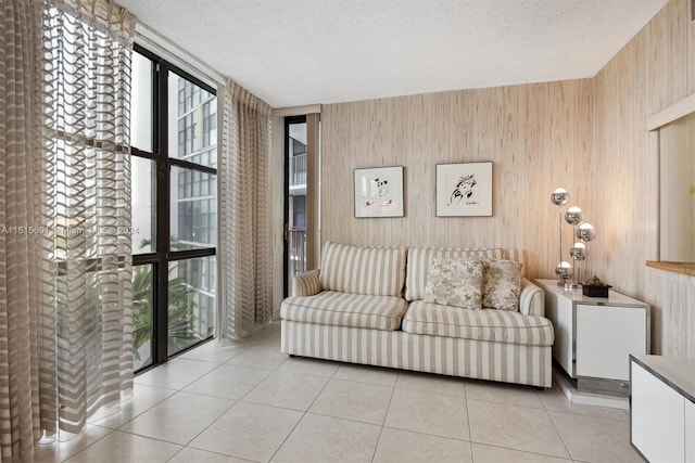 tiled living room with plenty of natural light, wood walls, expansive windows, and a textured ceiling