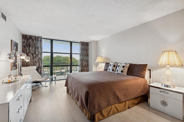 bedroom featuring a textured ceiling, light hardwood / wood-style floors, access to outside, and a wall of windows