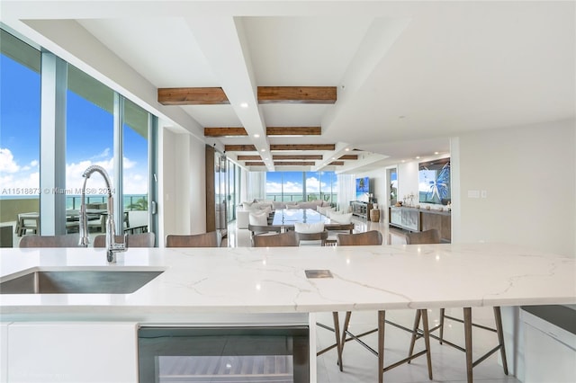 kitchen with coffered ceiling, light stone countertops, beamed ceiling, sink, and beverage cooler