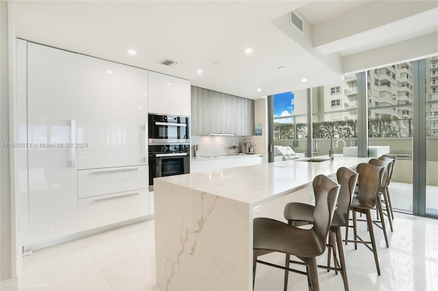 kitchen featuring double oven, light tile flooring, light stone countertops, a breakfast bar, and a center island with sink