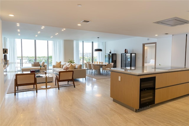 kitchen with wine cooler, a wall of windows, light stone countertops, and an island with sink